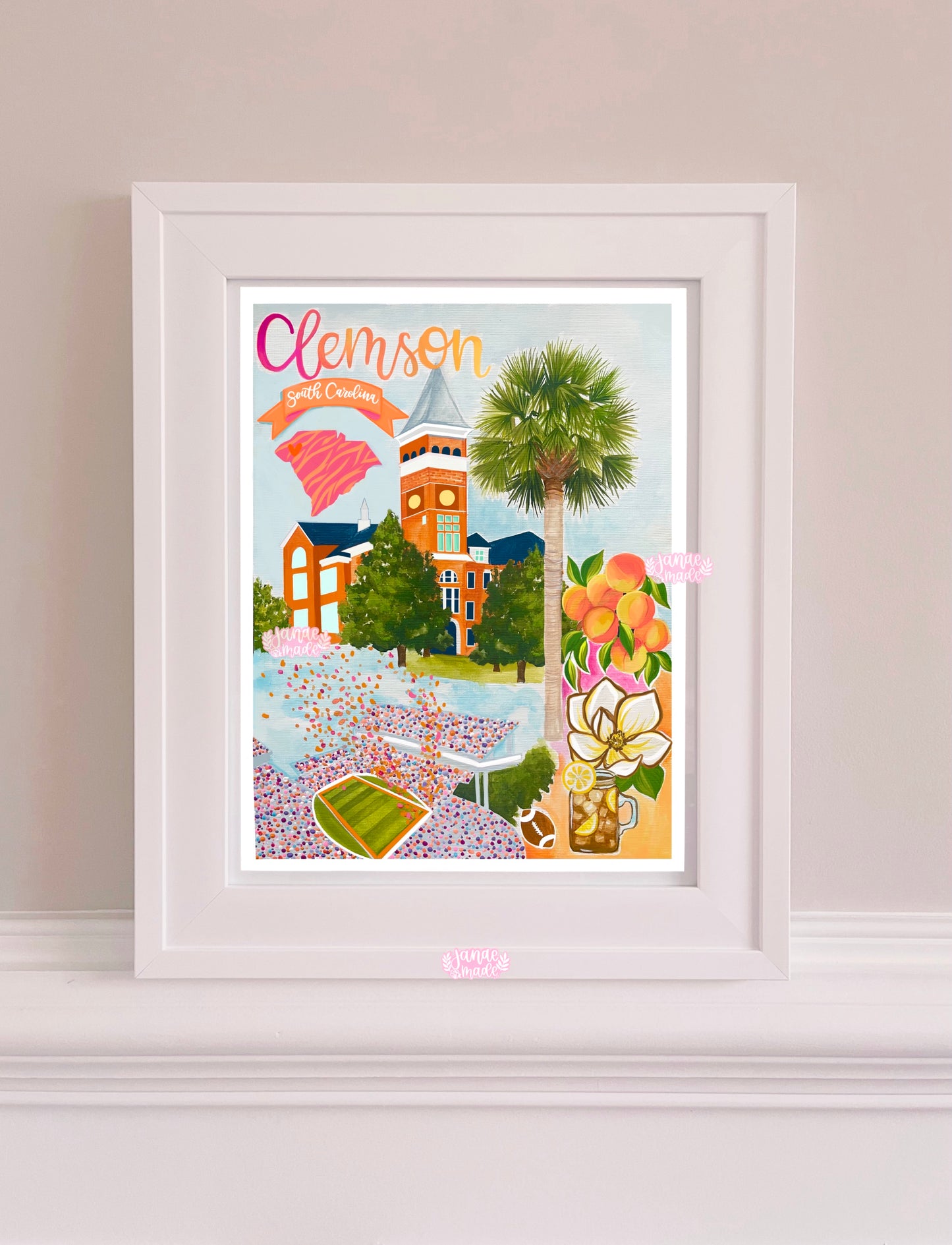 A colorful art print rests in a white frame featuring details unique to Clemson South Carolina. There is a palmetto, magnolia, a jar or sweet tea, and a football stadium.