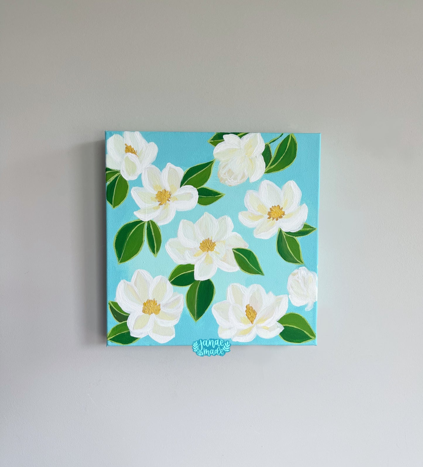 This is a patterned painting filled with cream colored magnolias and soft bright white outlining. Each magnolia has green leaves attached and a yellow center.