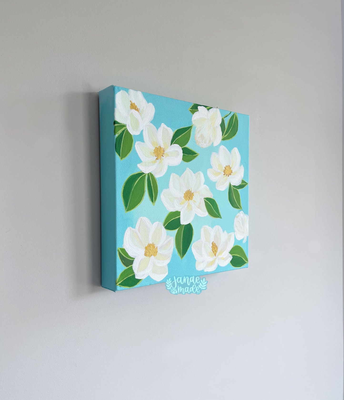 This is a patterned painting filled with cream colored magnolias and soft bright white outlining. Each magnolia has green leaves attached and a yellow center. Side view