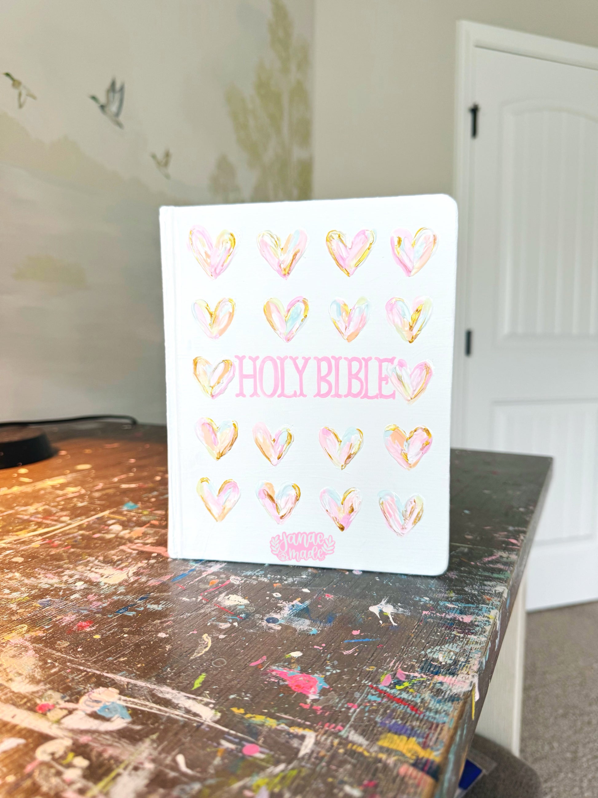 Colorful pastel textured hearts painted onto white background cover with "HOLY BIBLE" written in pink Fishtail font